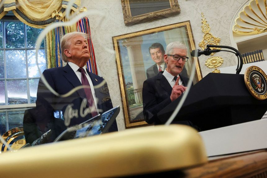 An engraved glass disc featuring Apple's logo that was presented to the president is seen in the forground as Apple CEO Tim Cook speaks during an event in the Oval office on August 6.  Apple announced a $100 billion investment in US manufacturing.