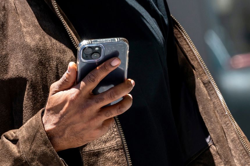 A pedestrian holds an iPhone in front of an Apple store in San Francisco, California, on June 11, 2024.