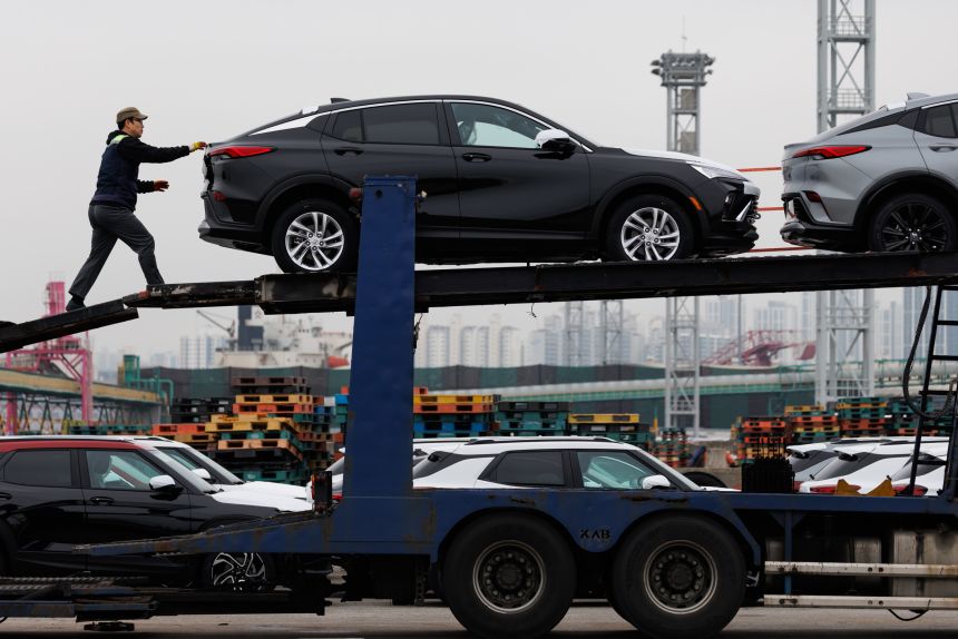 A worker prepares to unload General Motors Buick vehicles on a trailer truck at the Port of Incheon in Incheon, South Korea.