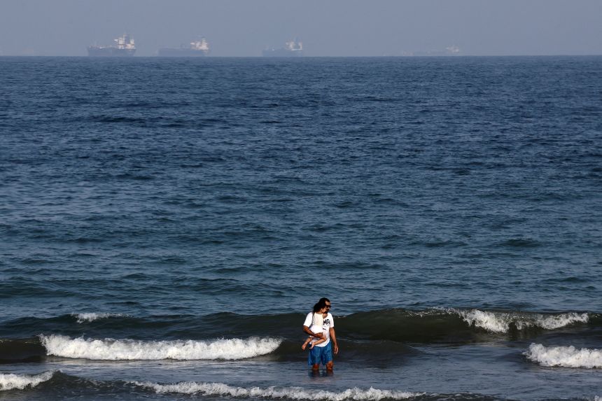 People stand in the water, with tankers in the background, as Iran vows to close the Strait of Hormuz, amid the US-Israel conflict with Iran, in Fujairah, United Arab Emirates, on March 3, 2026.