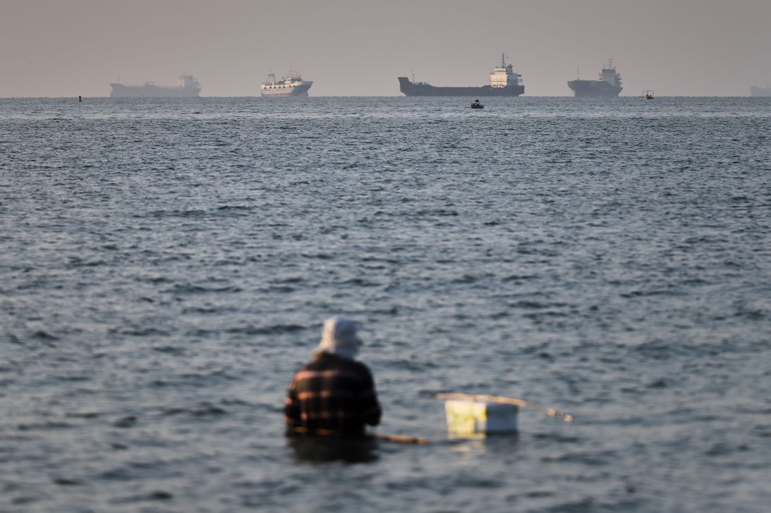 A person sits in shallow water as cargo and commercial vessels are anchored in the Strait of Hormuz off Bandar Abbas, Iran, Monday, June 8, 2026.