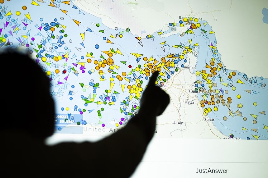 A photo illustration shows a person in front of a large screen displaying vessel movements in the Strait of Hormuz on a ship-tracking website on May 4, 2026.