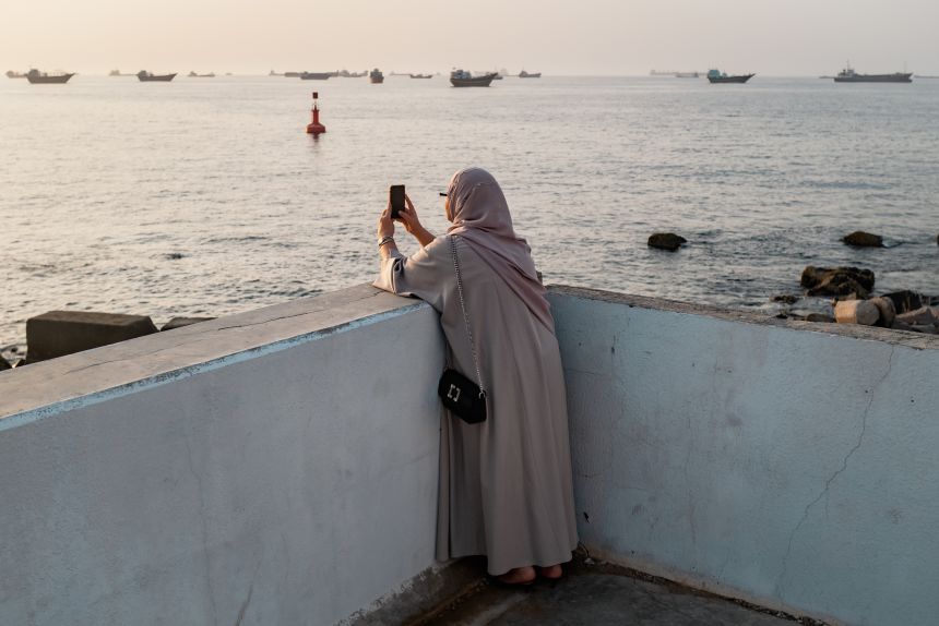 An Omani woman photographs Qaboos Port where oil tankers, carriers, vessels and Omani fisherboats sit anchored on Friday.